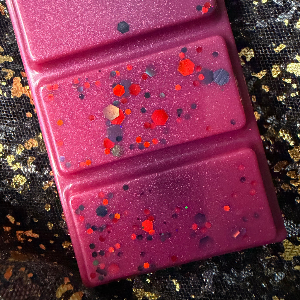 Detailed photograph of two Theo de Fangle segments showing red circles, dark glitter and small orange pieces scattered across the magenta wax.