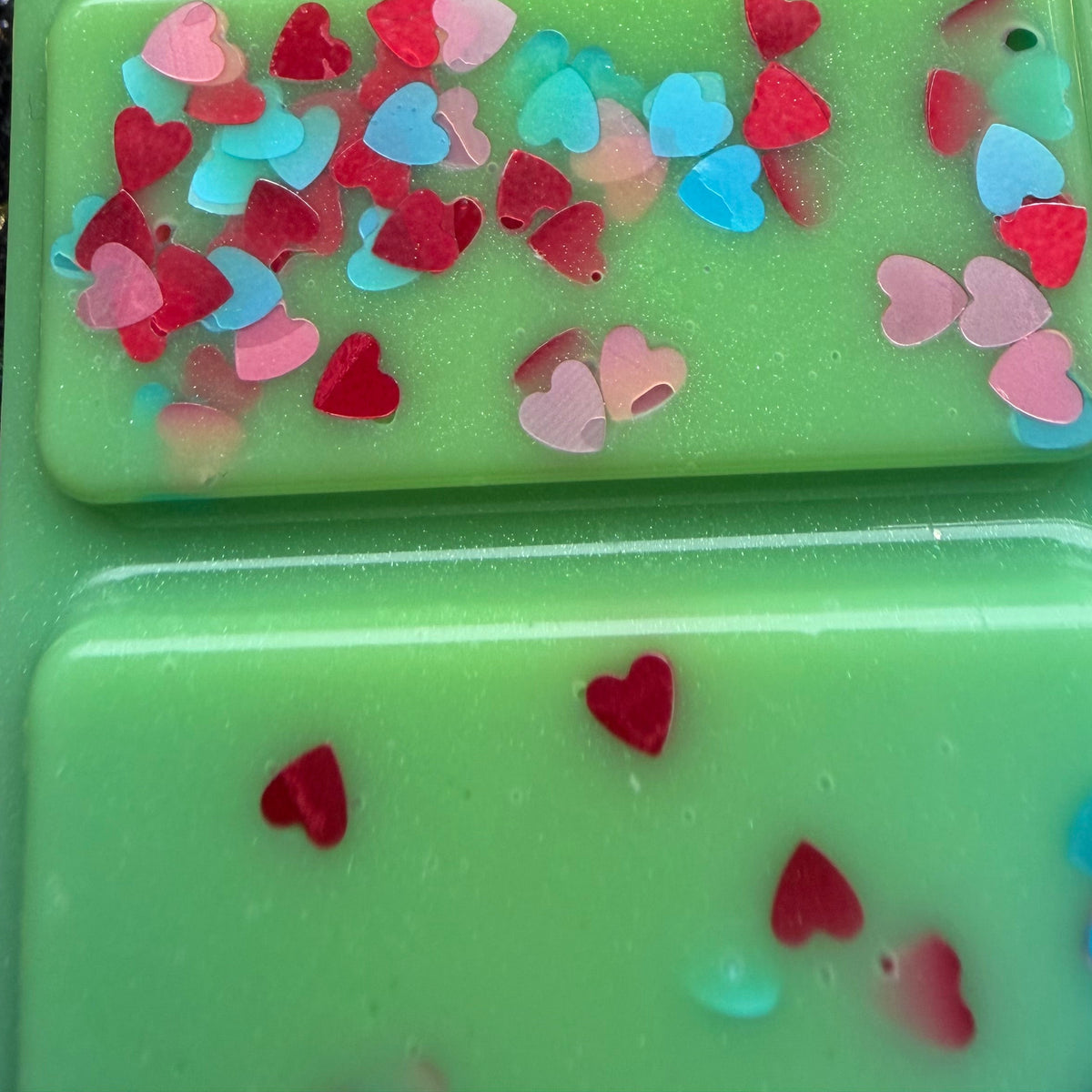 Close-up of the spring-green Lady Bridgerton’s Garden vegan soy wax melt showing clusters of red, pink and blue heart-shaped confetti across two raised segments.