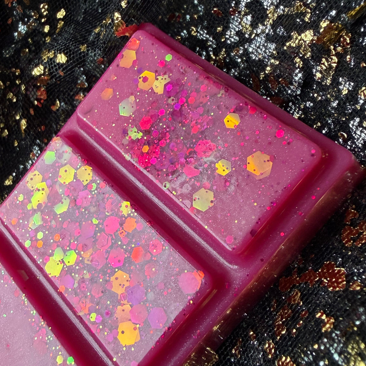 Close-up of HMS Blossom flower bomb scented soy wax melt segments showing gold, yellow and iridescent hexagonal glitter against vivid pink wax.
