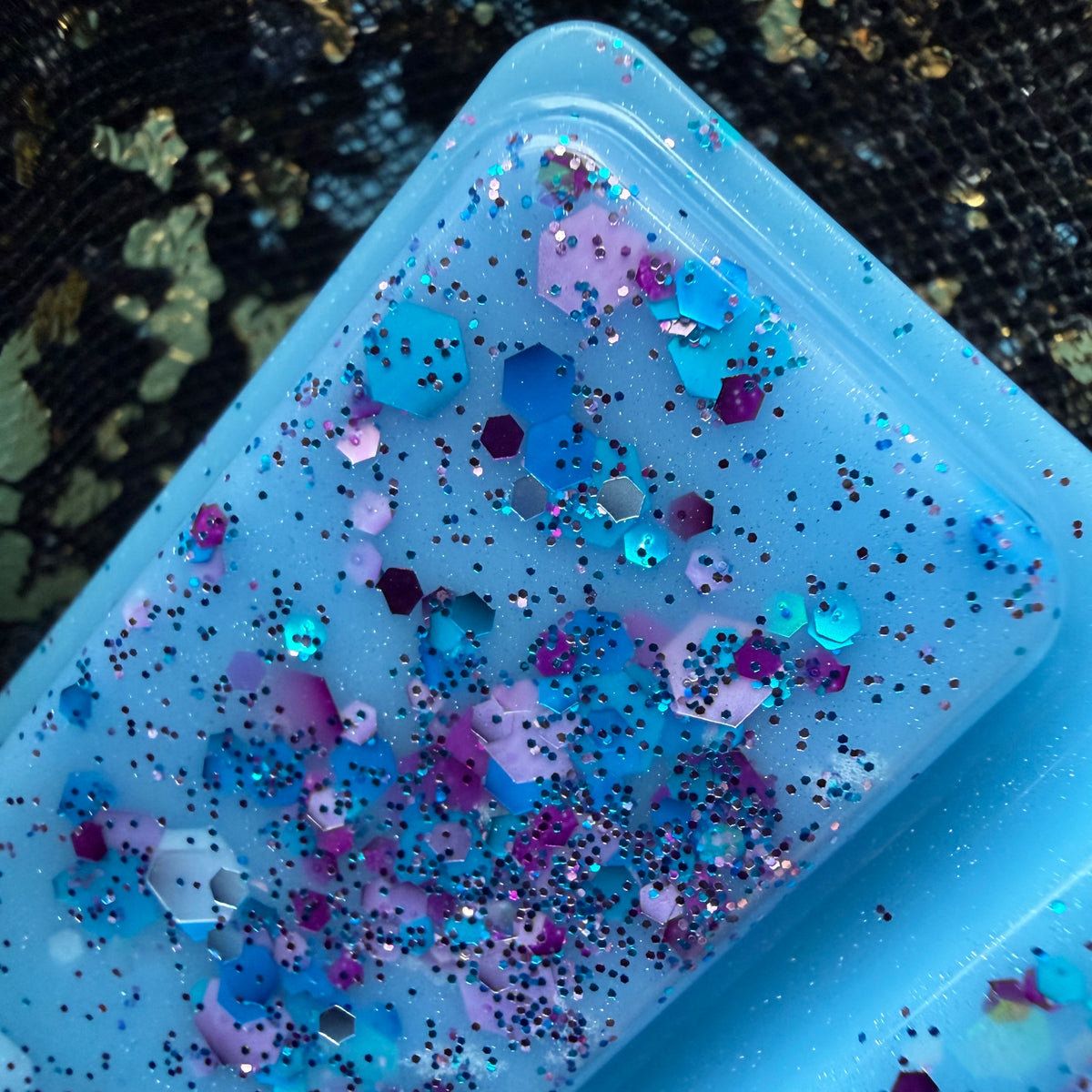 Zoomed-in photograph of a Starfall segment showing concentrated pink, purple, turquoise and silver glitter against the blue wax.