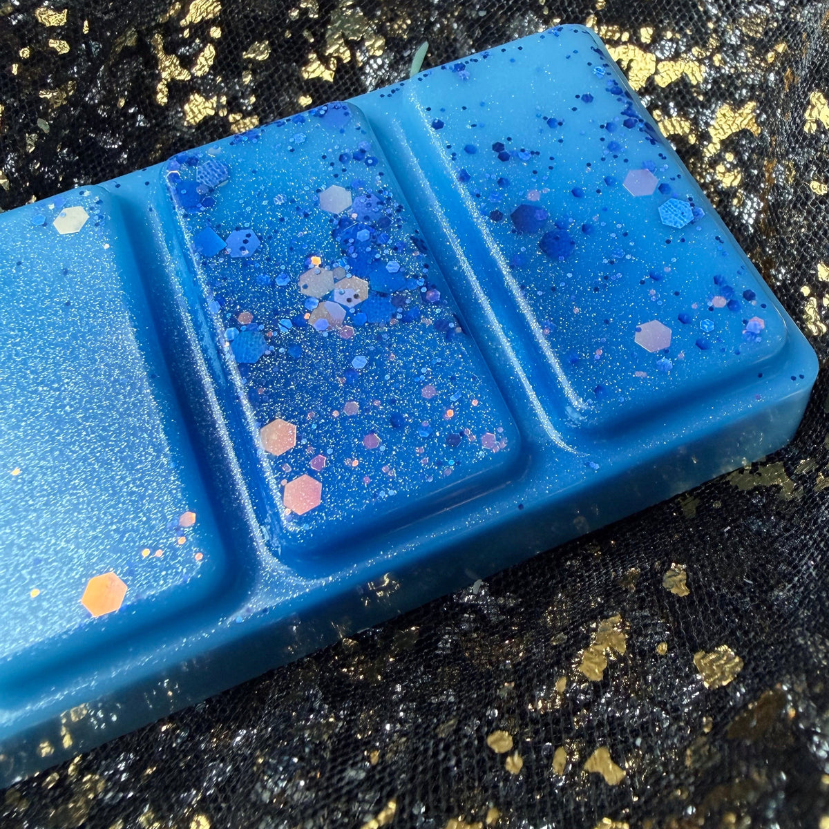 Close-up of three Snowy Escape wax melt segments showing purple, pink and silver glitter scattered across vivid blue wax.