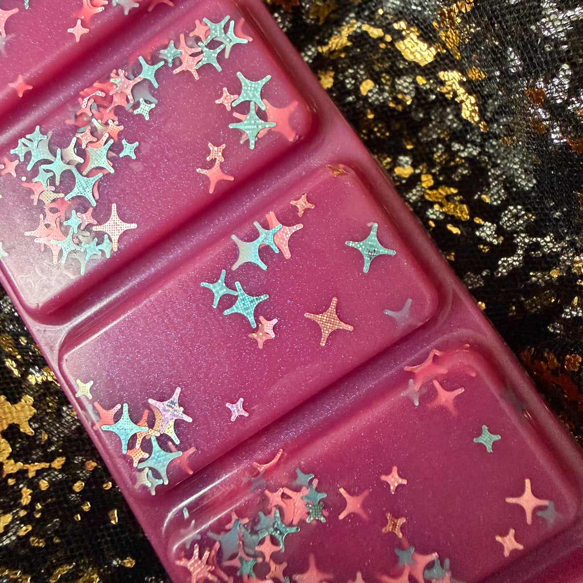 Zoomed-in photograph of the One More Chapter wax melt showing overlapping holographic stars reflecting blue, green, pink and silver.