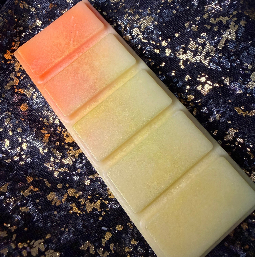 Full-length Honeybee vegan soy wax melt positioned diagonally on black-and-gold fabric, showing the orange-to-honey-yellow gradient across all five rectangular segments.