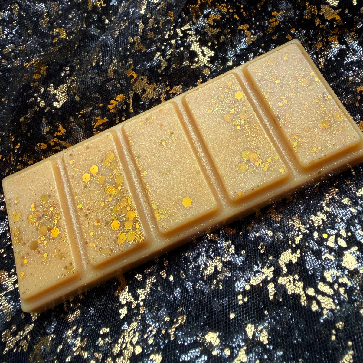 Side view of Roary Night’s five segment golden wax melt, with its long outer edge visible beneath fine shimmer and scattered gold hexagonal glitter.