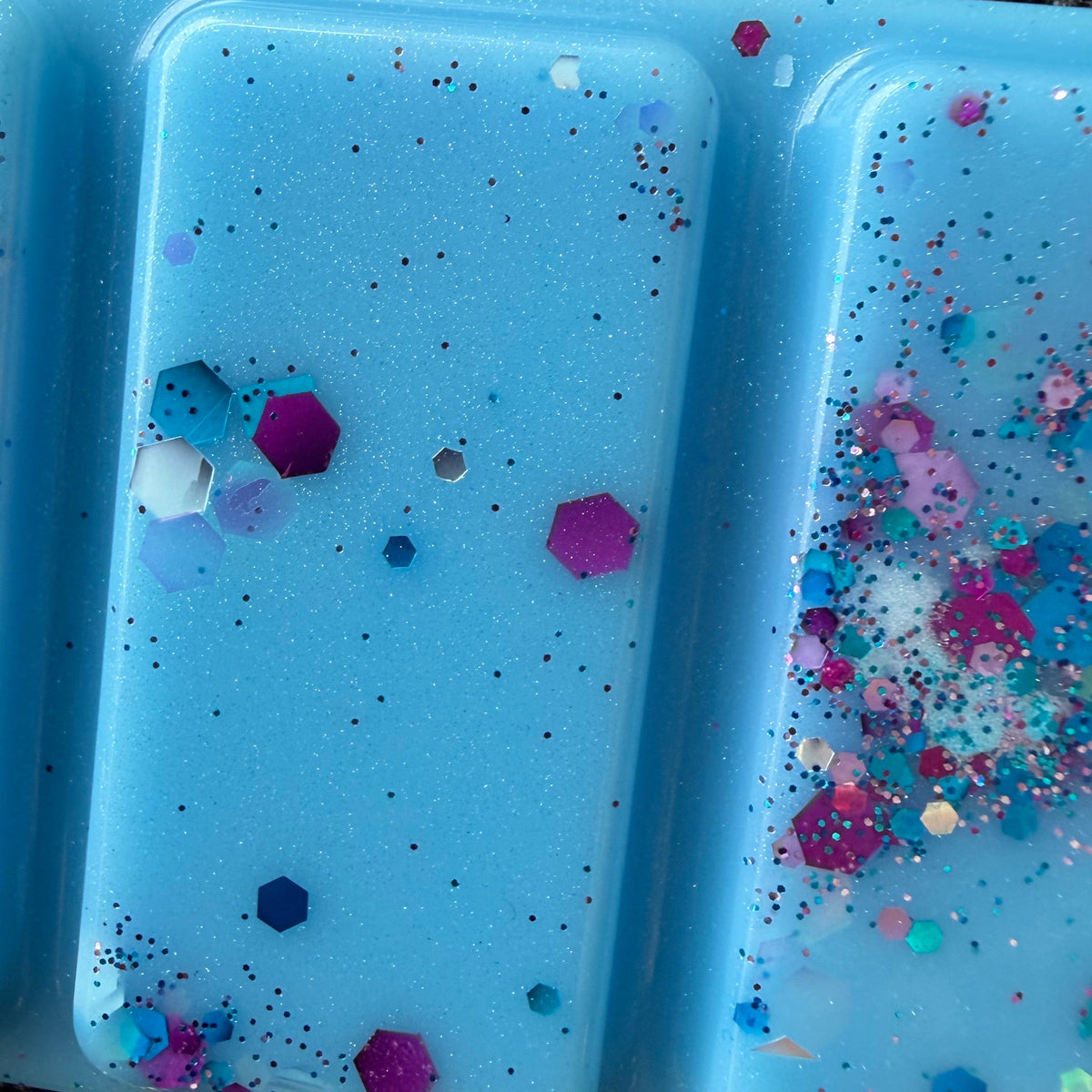 Detailed photograph of the Starfall wax melt showing larger pink and purple hexagonal glitter beside fine silver and blue pieces.