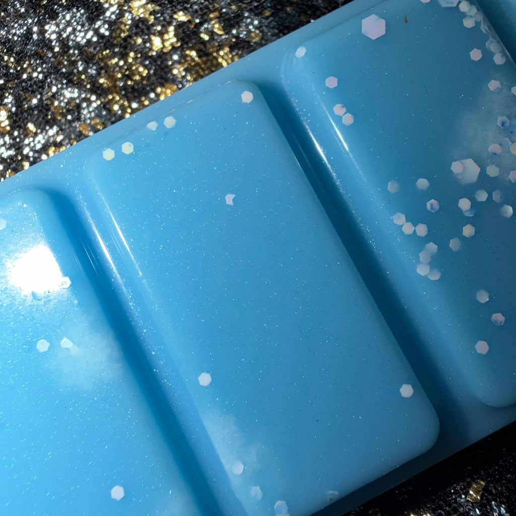 Close-up of two Cleaning Fairy wax melt segments showing white and silver glitter scattered across the bright blue wax.