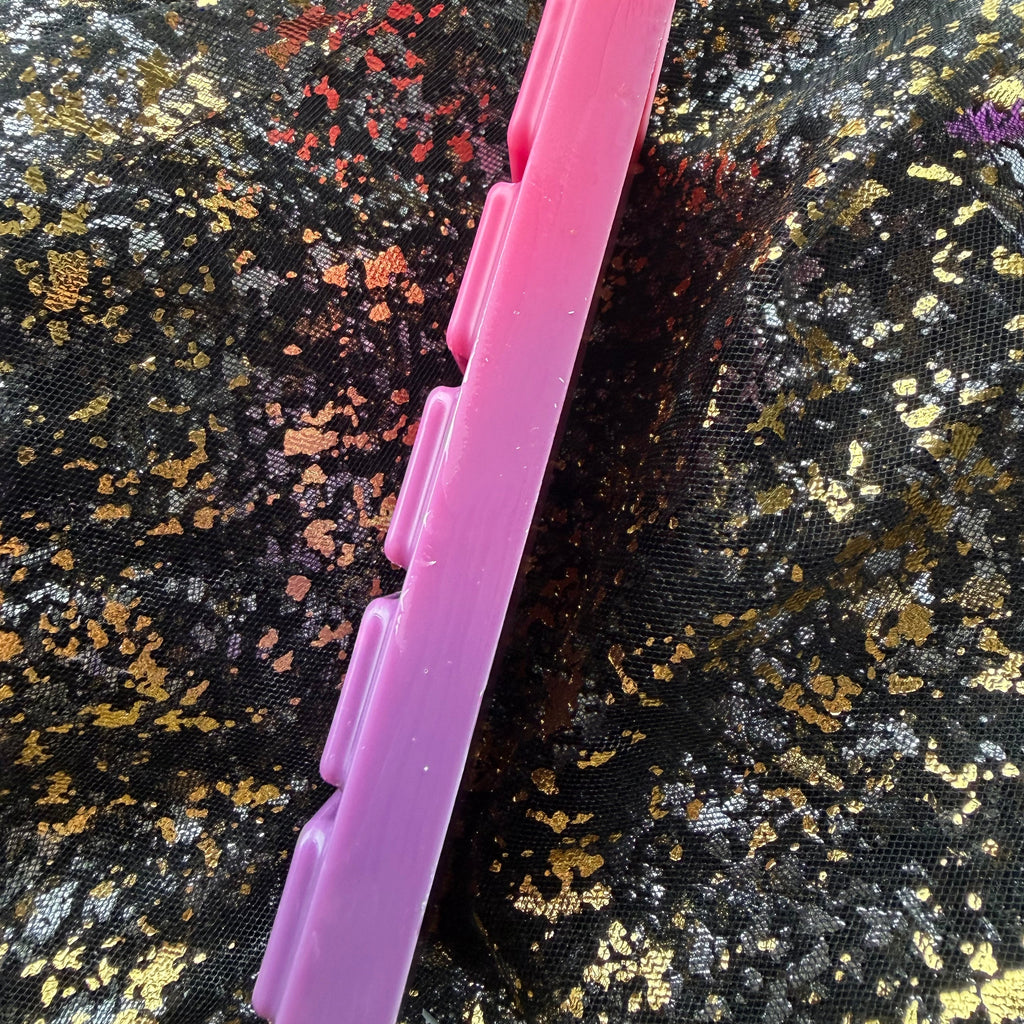 Side-profile photograph of The Midnight Wish wax melt showing the slim edge of the pink five-segment bar against black-and-gold fabric.
