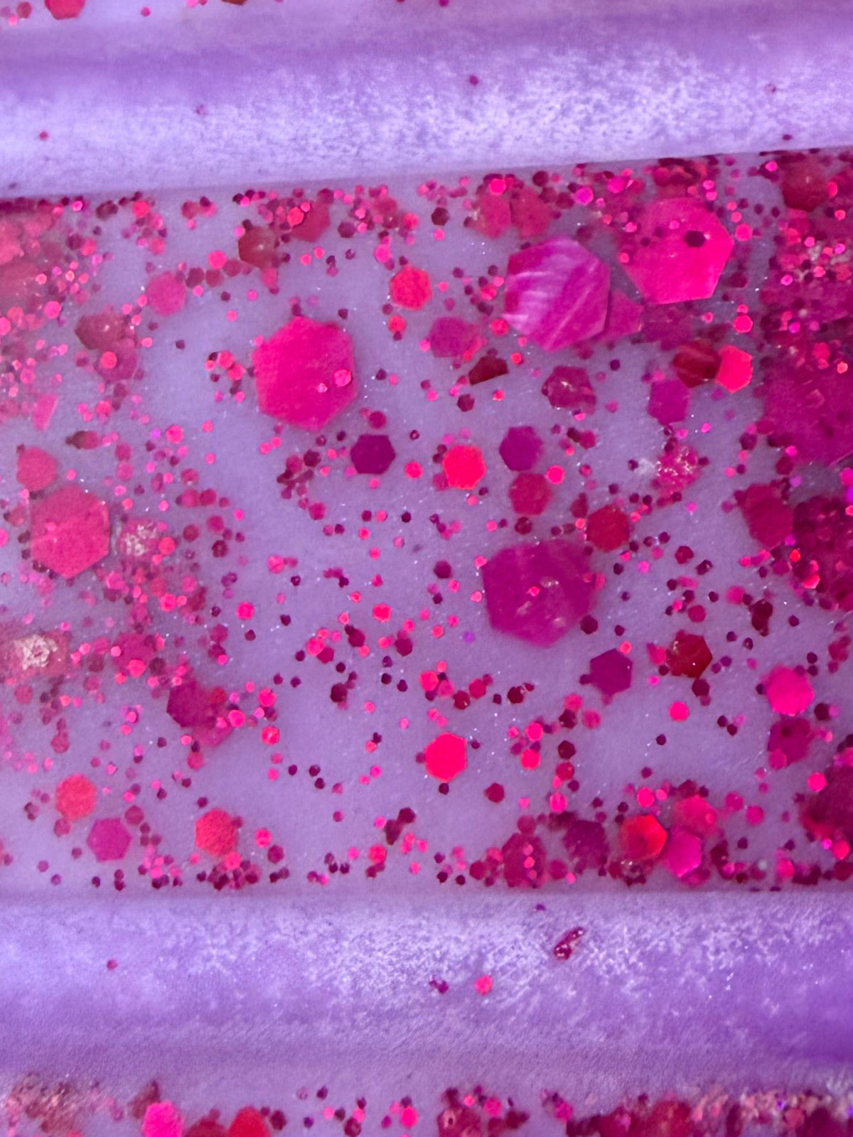 Zoomed-in view of one pale lilac Cherries on Snow wax melt segment decorated with fine pink glitter and larger bright pink hexagons, photographed between the raised segment lines.
