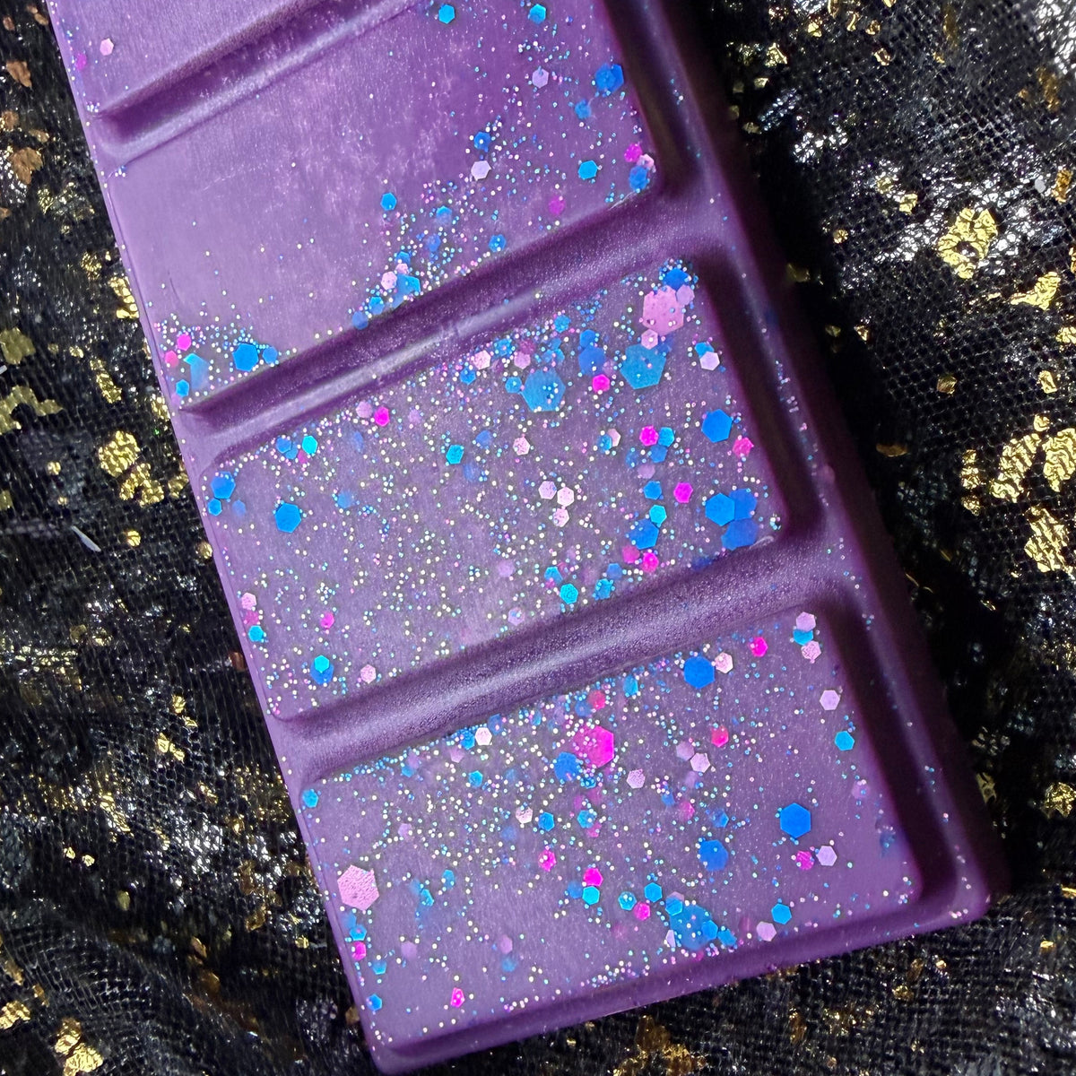 Close up of deep purple coloured blackberry and bay leaf scented soy wax melt displaying the purple, pink and blue glitter. 