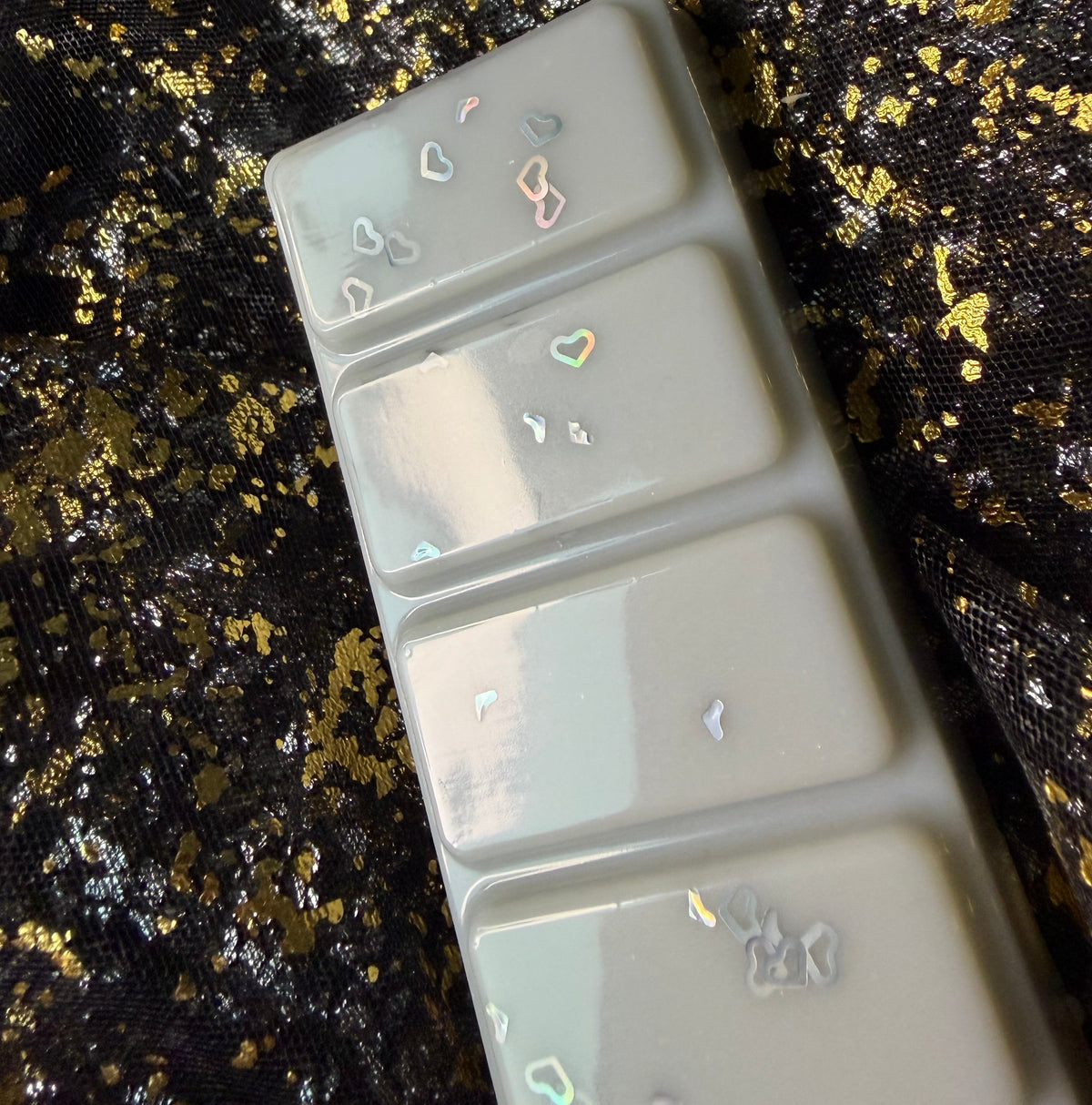 Fallen Angel five-segment book-inspired wax melt positioned sideways beside its labelled clamshell on a black and gold fabric background.