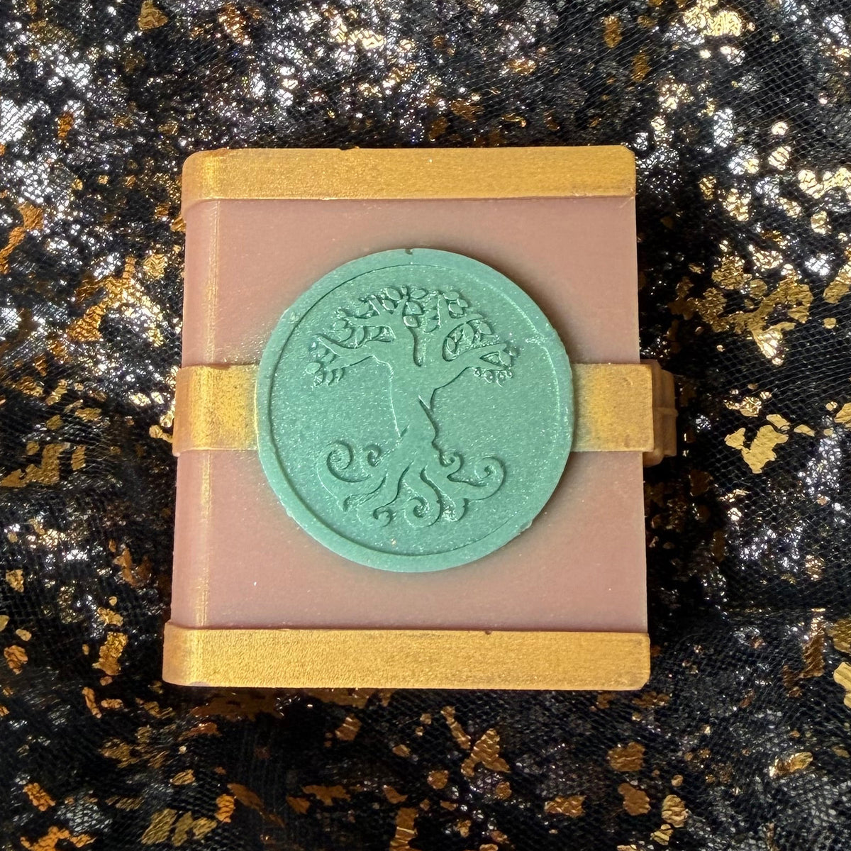 Close view of the Earth spellbook wax melt, with the tree’s leaves and curled roots visible on its shimmering mint green circular emblem.