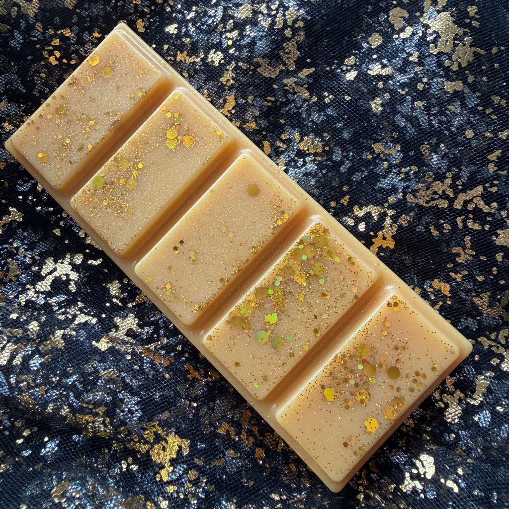 Roary Night gingerbread wax melt displayed diagonally on black and gold fabric, with five pale cream gold sections and iridescent glitter clustered towards one end.