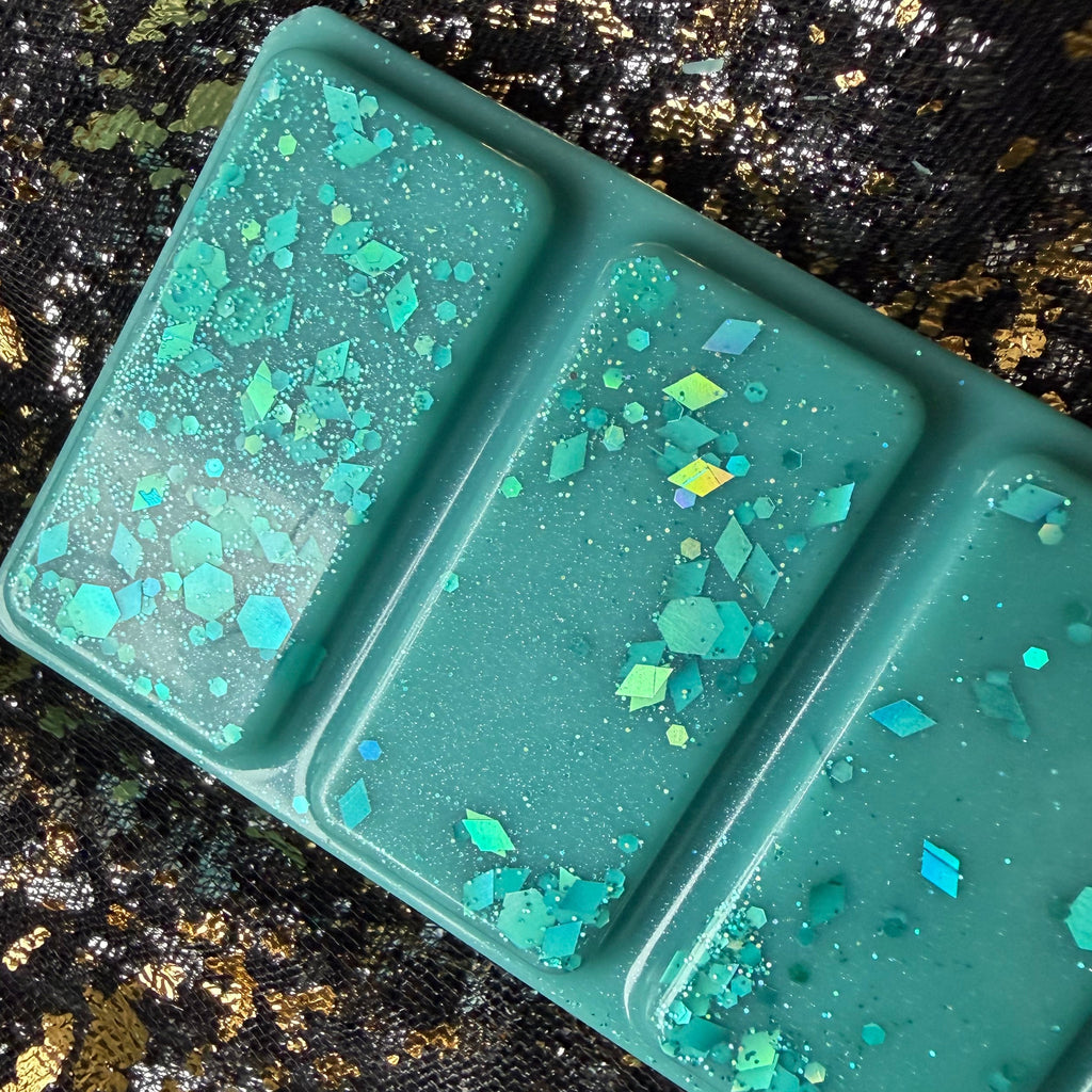 Close-up of the upper Malibu tropical scented wax melt segments, showing turquoise wax decorated with blue, silver and iridescent glitter flakes.