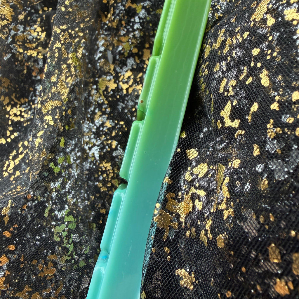 Side-profile photograph of the Lady Bridgerton’s Garden wax melt showing the slim five-segment bar and its green-to-turquoise colouring against black-and-gold fabric.
