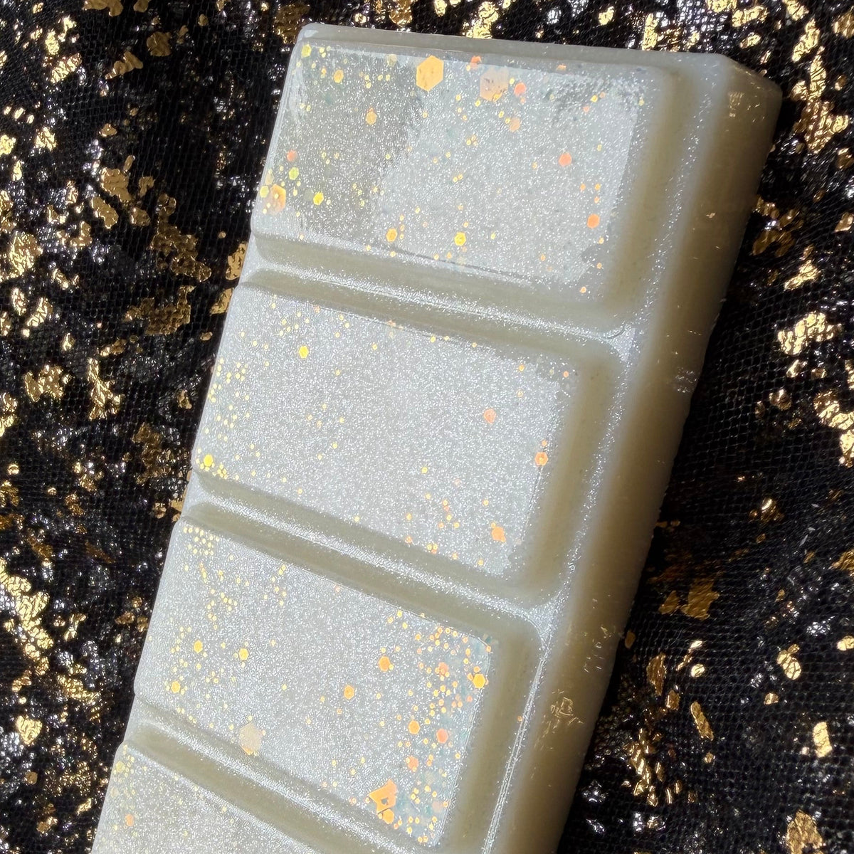 Close view of the upper sections of Xavier Acrux’s ivory wax melt, with fine silver shimmer and peach gold hexagonal glitter beside the visible right edge.