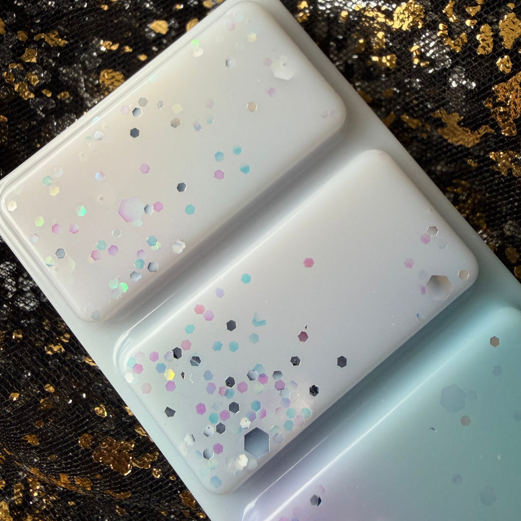 Close-up of three Spring Court wax melt segments showing pastel blue, creamy white and pale lilac colouring with fine multicoloured glitter.