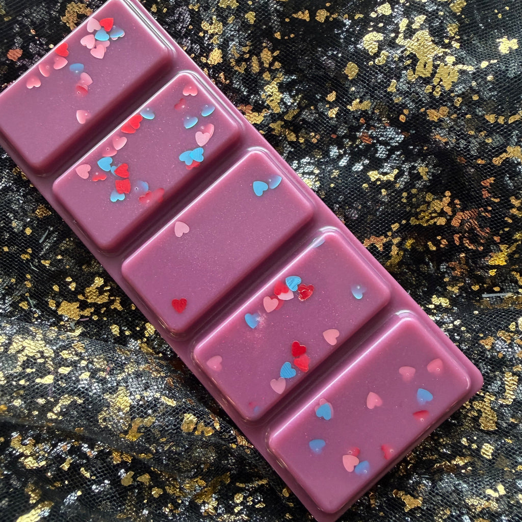 Bryce After Dark bookish wax melt, shown sideways as a deep berry-purple rectangular five-segment soy wax bar decorated with multicoloured heart-shaped glitter on black-and-gold fabric.