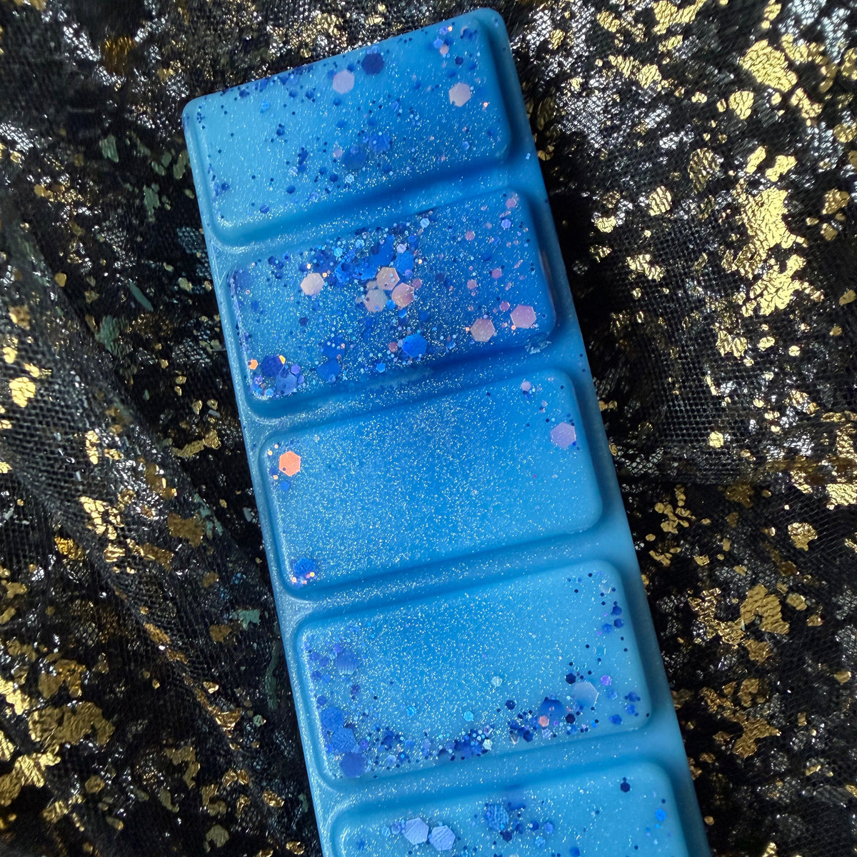 Full-length Snowy Escape wax melt positioned vertically on black-and-gold fabric, showing all five vivid blue rectangular segments.