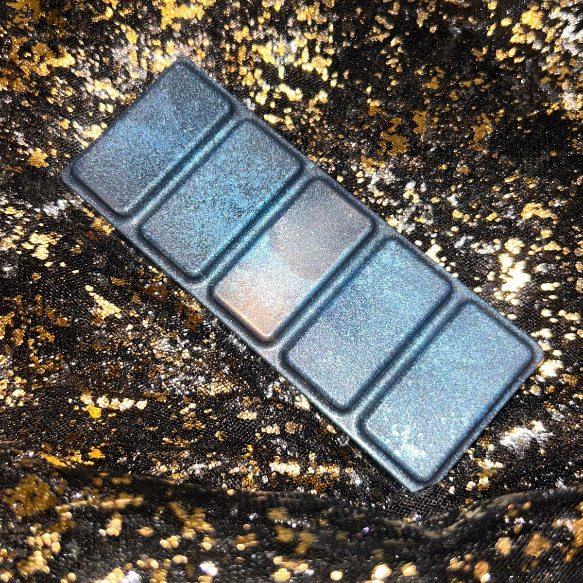 Overhead photograph of the unpackaged Darcy Vega wax melt, extending from the upper left to the lower right, with five dark blue rectangular sections covered in fine silvery blue shimmer.