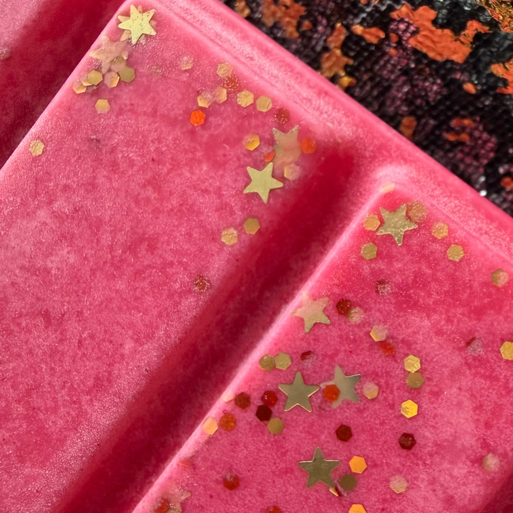 Close-up of two red Love & Luck wax melt segments, showing metallic gold stars, small gold circles and fine sparkling glitter.