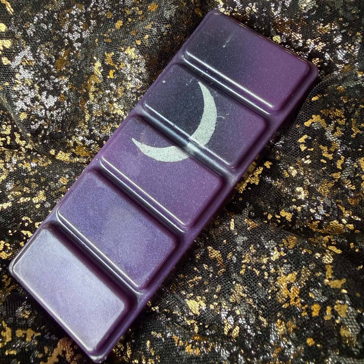 Angled photograph of the Lord of Shadow and Blood five-segment wax melt, showing its rich purple colouring, fine shimmer and silver moon decoration.