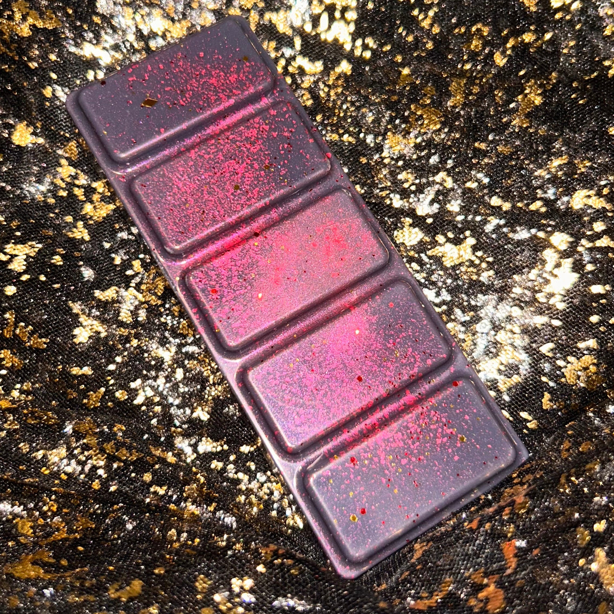Tory Vega five segment wax melt displayed diagonally on black and gold fabric, with bright red shimmer across the dark burgundy wax.