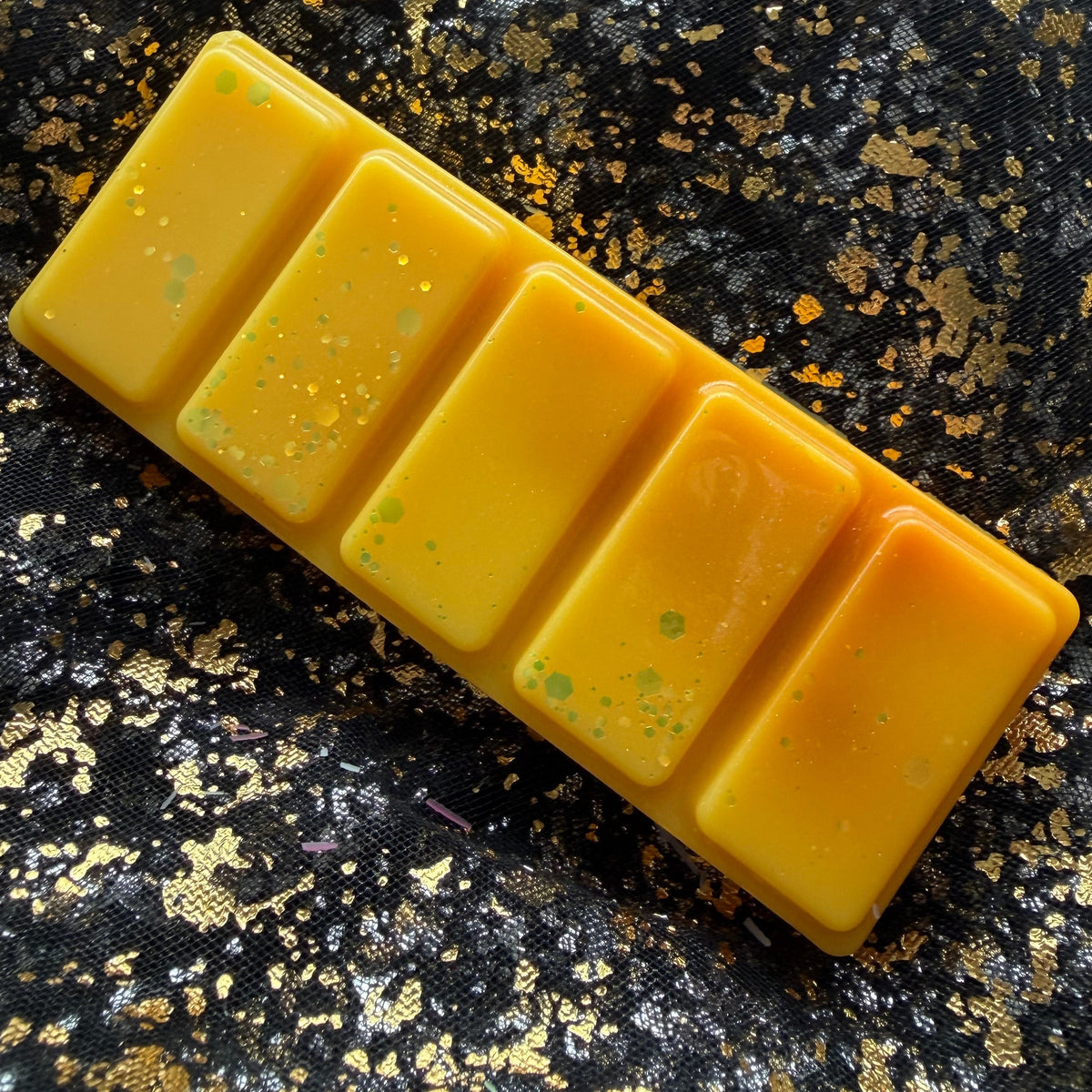 Full-length Summer Slow Burn wax melt positioned diagonally on black-and-gold fabric, showing all five golden-yellow rectangular segments.