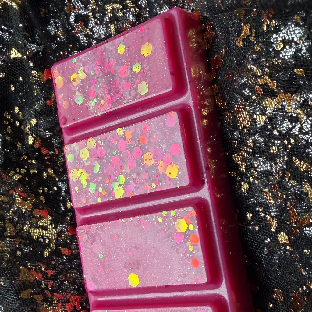Close-up of two HMS Blossom wax melt segments showing gold, yellow and iridescent hexagonal glitter against vivid pink wax.