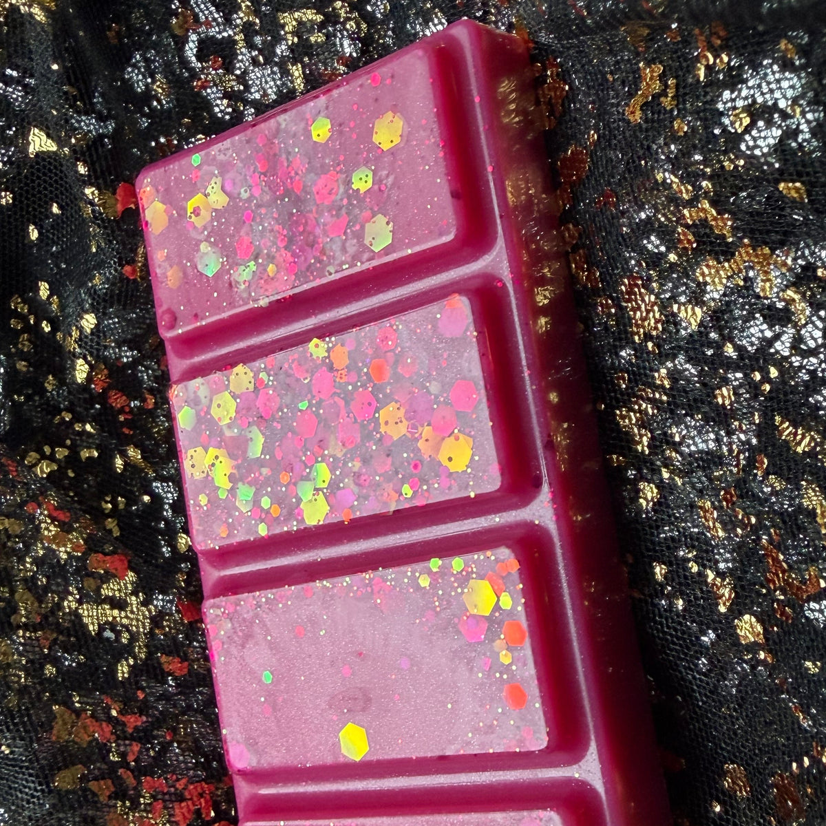 Close-up of two HMS Blossom wax melt segments showing gold, yellow and iridescent hexagonal glitter against vivid pink wax.