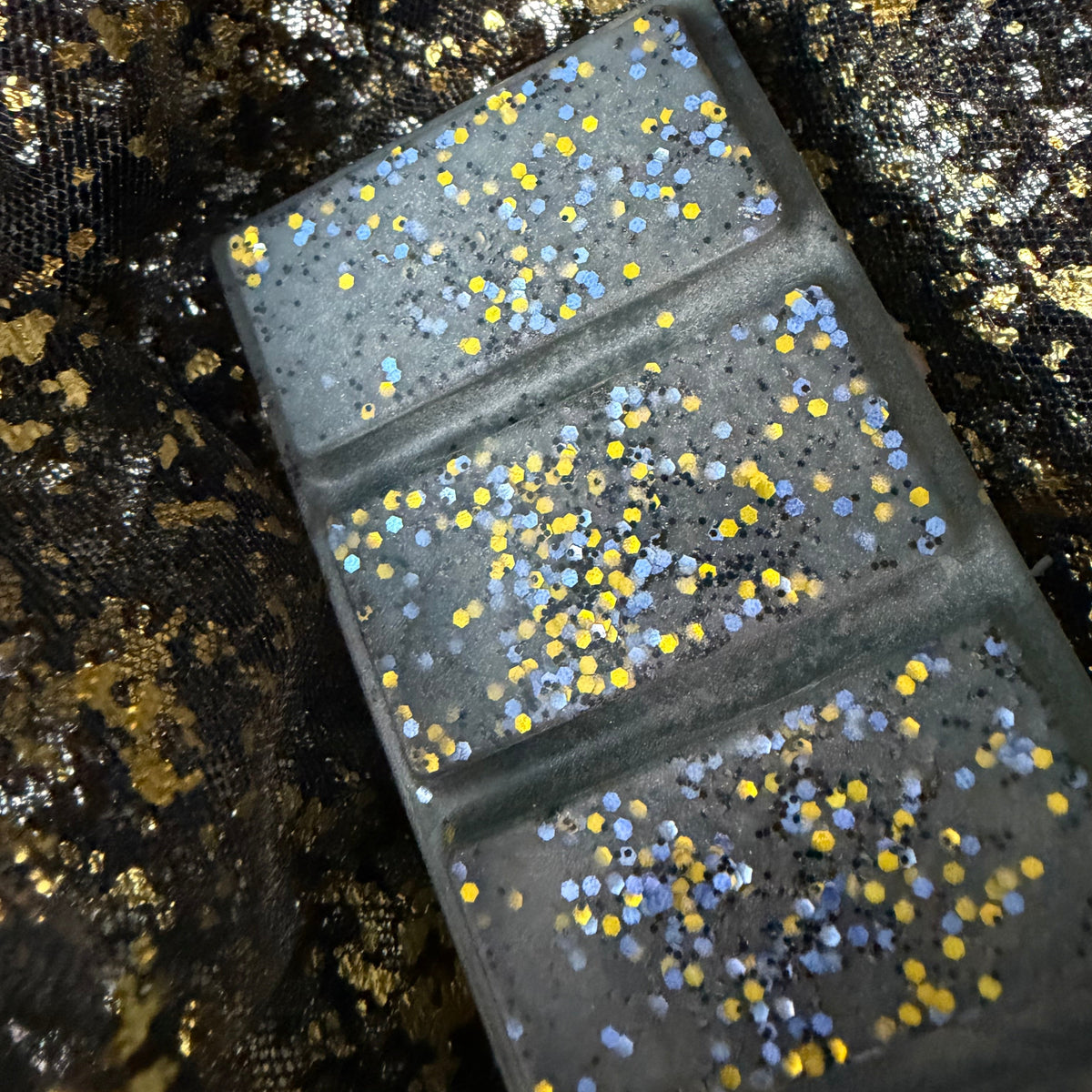 Close-up of three Shadow Daddy wax melt segments showing dense metallic gold, silver and yellow glitter against charcoal-grey wax.