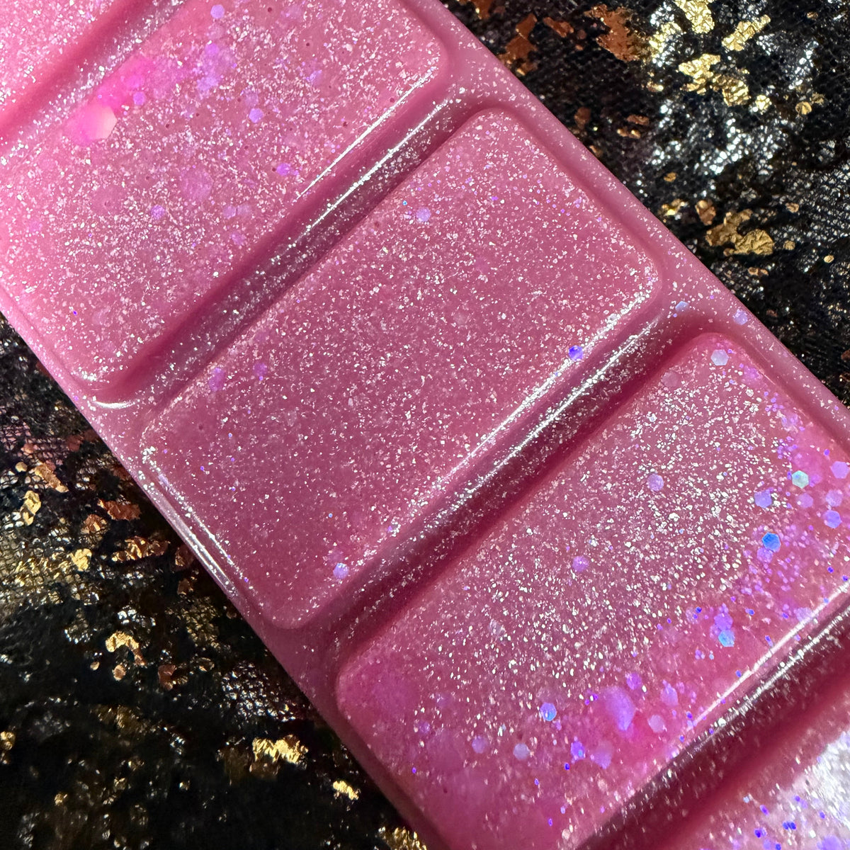 Close-up of the middle sections of the Flawless pink wax melt, showing dense silver shimmer, fine iridescent glitter and scattered pink and holographic confetti against black-and-gold fabric.