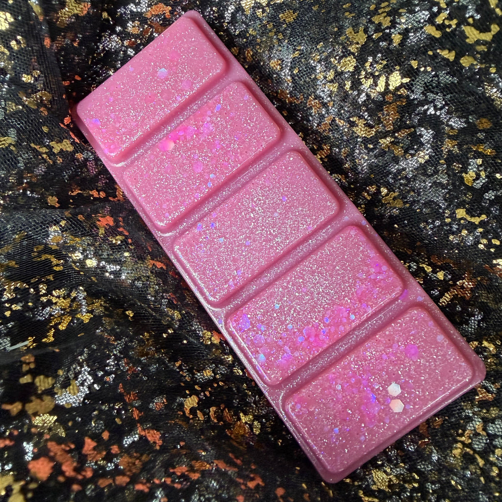 Full-length Flawless cowboy romance wax melt positioned diagonally on black, gold and copper fabric, showing all five pink rectangular segments decorated with silver shimmer and pink iridescent glitter.