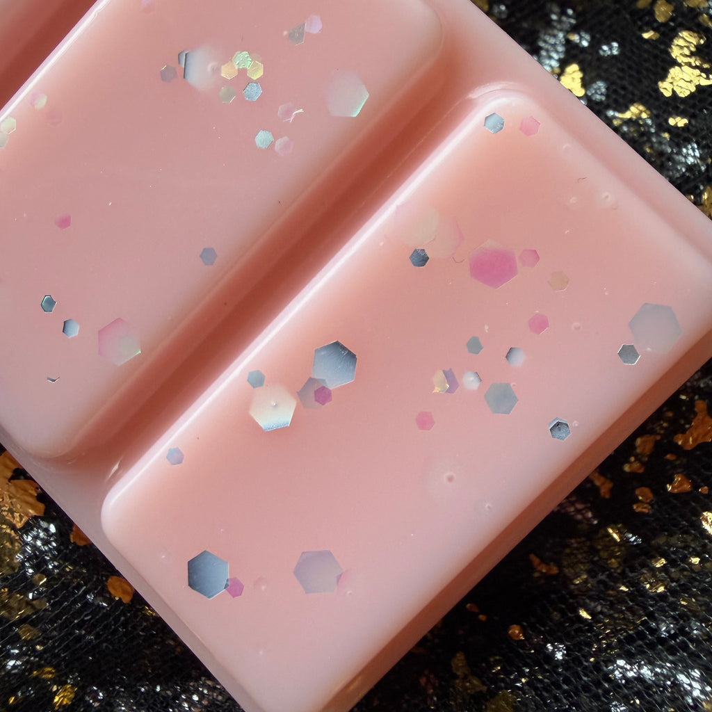 Close-up of two Peachy Keen wax melt segments showing smooth peach-pink colouring and scattered pastel and holographic glitter pieces.