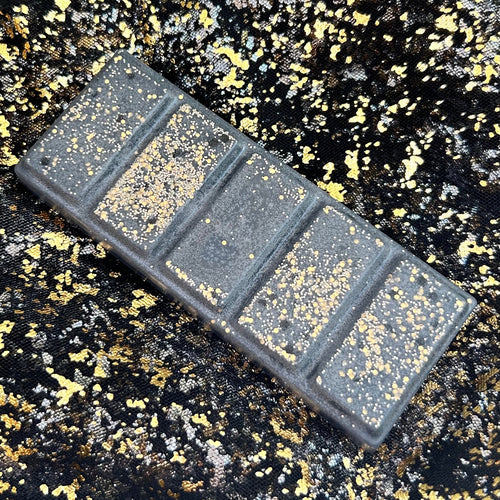 side view image of a black coloured soy wax melt decorated with gold glitter, scented with fruit, pomegranate and champagne