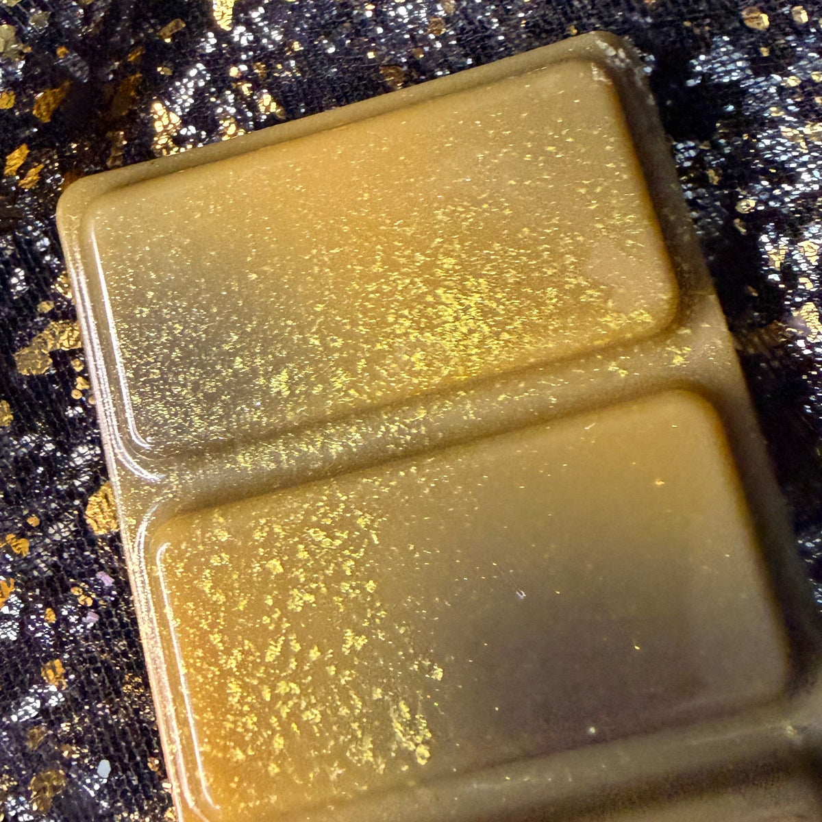 Close-up of two Lady of Light and Death wax melt segments showing blended olive and charcoal colouring covered with fine metallic golden shimmer.