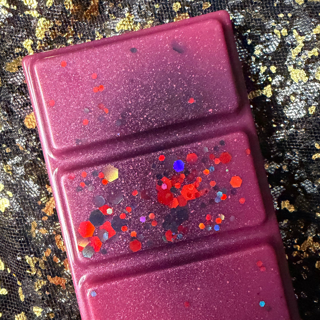 Close-up of two Theo de Fangle wax melt segments showing red, orange and charcoal glitter against deep magenta wax.
