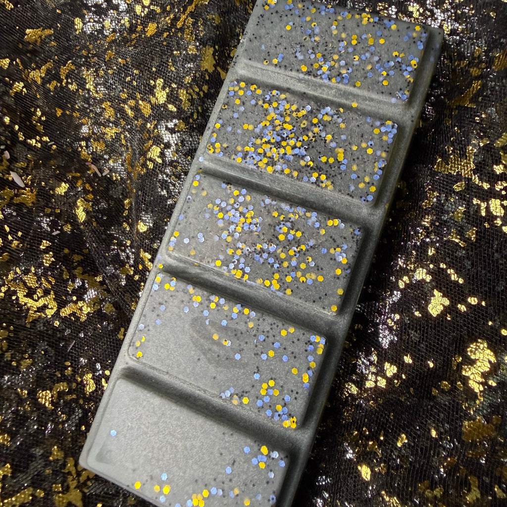 Full-length Shadow Daddy romantasy wax melt positioned diagonally on black-and-gold fabric, showing all five charcoal-grey segments and metallic glitter decoration.
