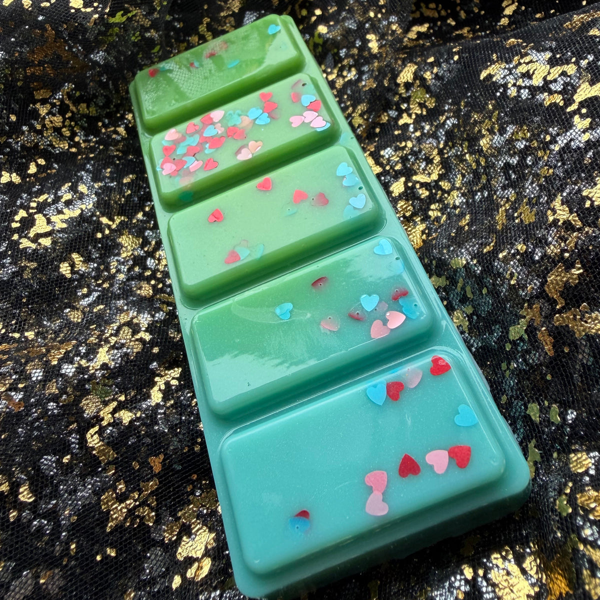 Green and turquoise Lady Bridgerton’s Garden mandarin and spring floral scented soy wax melt photographed from an elevated angle, showing pink, red and blue heart confetti across all five rectangular segments.