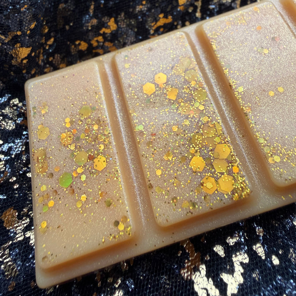 Close view of three Roary Night wax melt sections, with fine gold shimmer and larger hexagonal glitter reflecting gold and green against the pale golden wax.