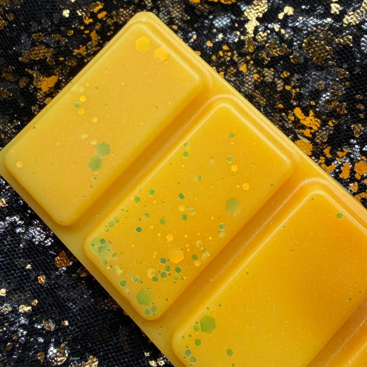 Angled photograph of two Summer Slow Burn segments showing green glitter pieces against the warm golden-yellow colouring.