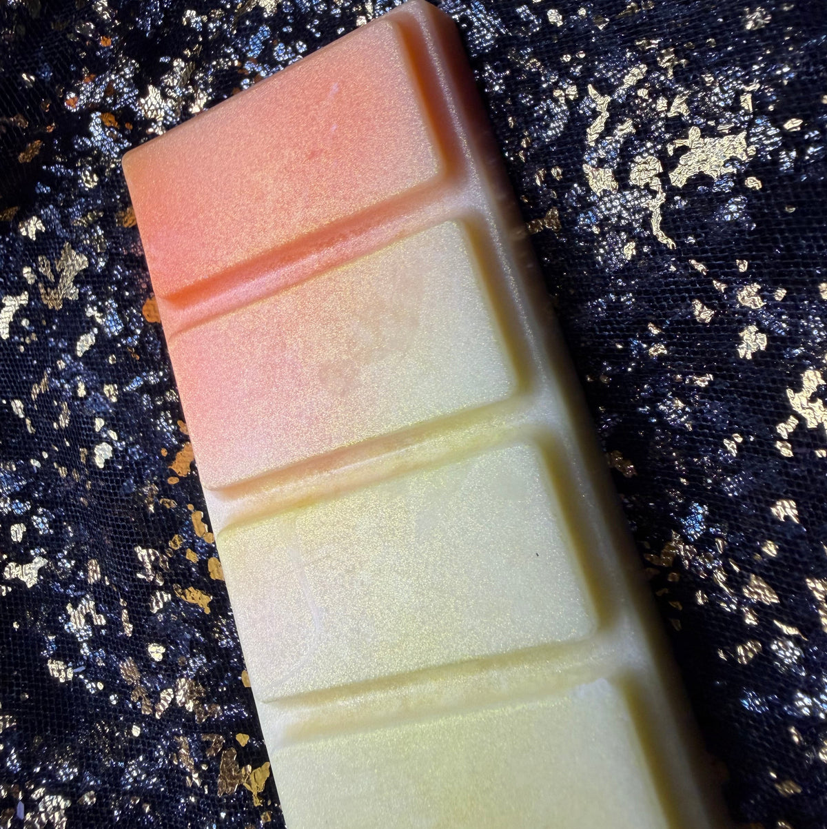 Angled photograph of the Honeybee five-segment wax melt showing its orange upper section, creamy yellow lower sections and fine golden shimmer against black-and-gold fabric.