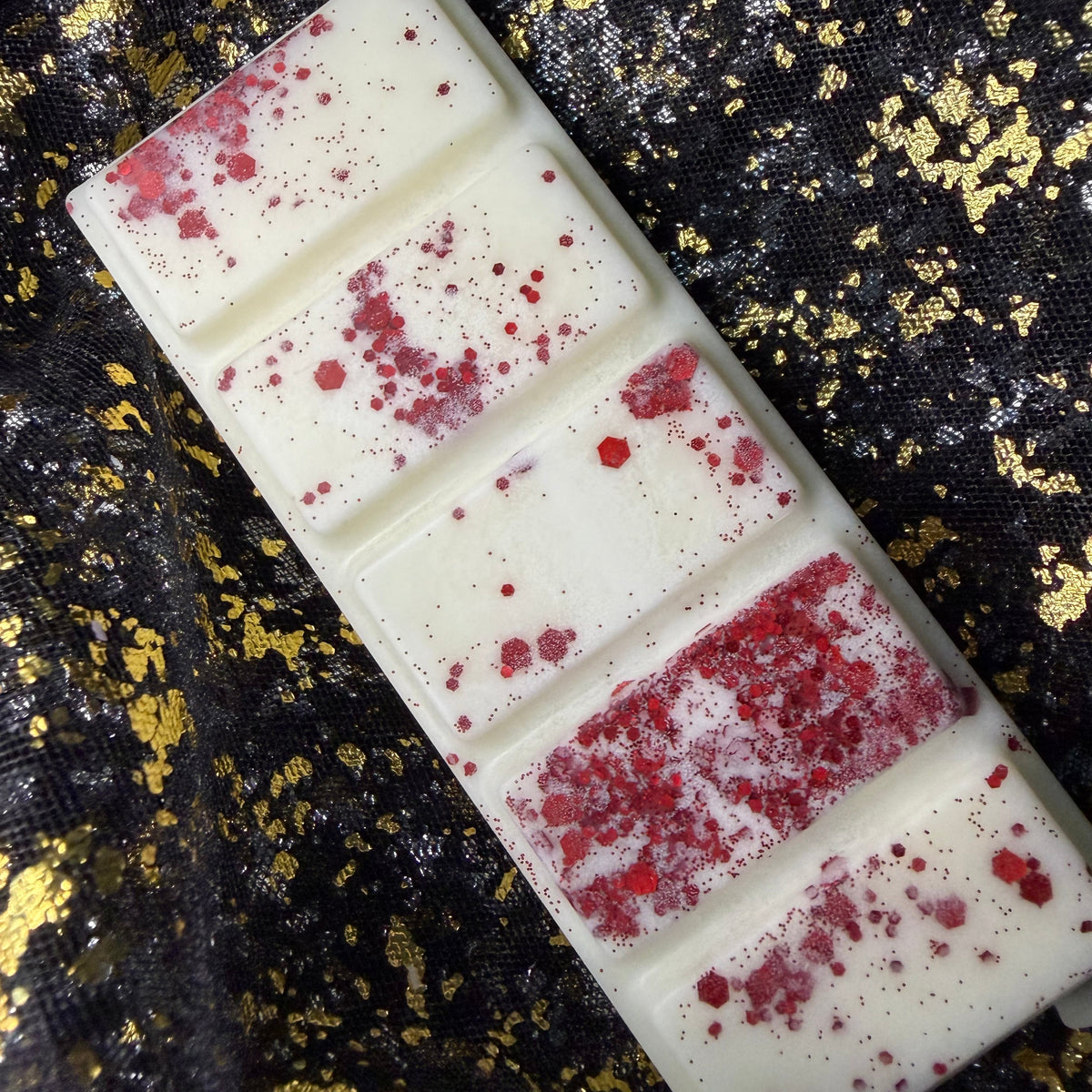 Side-angled photograph of the Forbidden Fruit five-segment ivory wax melt, showing the raised rectangular sections and an uneven scattering of fine red glitter, red flakes and hexagonal pieces.