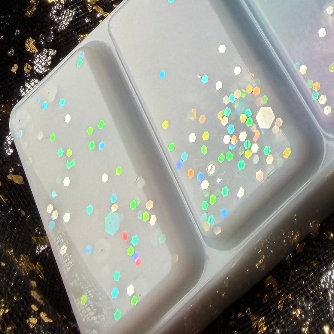 Detailed photograph of two Spring Court segments showing pink, green, yellow and blue iridescent glitter against creamy white and pastel blue wax. Long lasting fresh linen scented soy wax melts. 