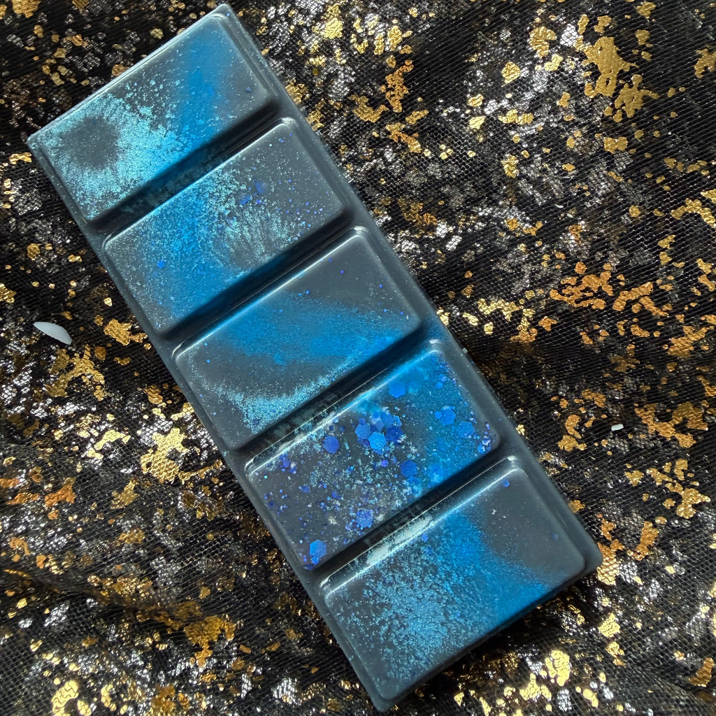 Darcy Vega five segment soy wax melt lying diagonally on black and gold fabric, showing a vivid blue streak, patches of turquoise shimmer and blue hexagonal glitter clustered on the fourth segment from the top.