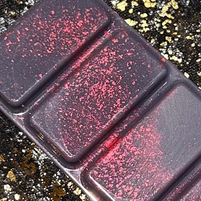 Close view of the middle segments of Tory Vega’s burgundy red and black wax melt, with red shimmer and scattered gold glitter across the wax.