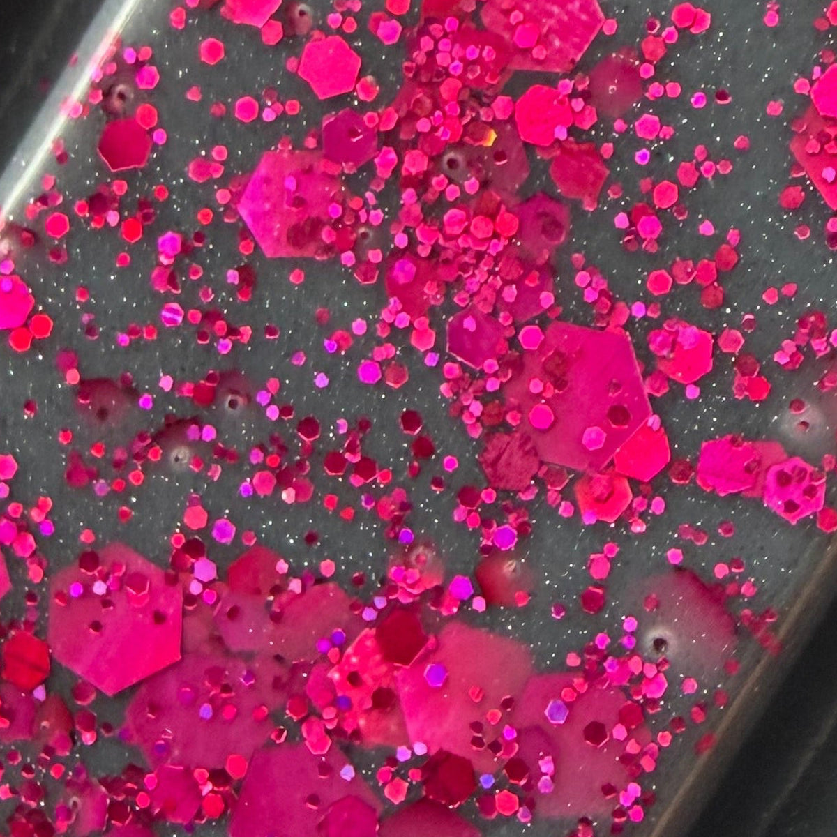 Zoomed-in photograph of The Black Beak Witch wax melt showing fine pink shimmer, circular glitter and larger irregular pink flakes.