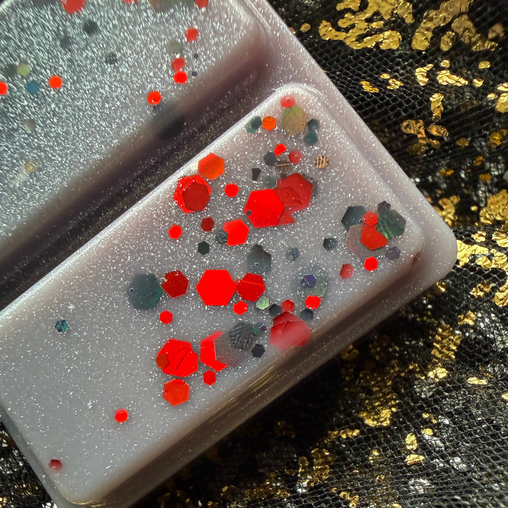 Close-up of two segments of Thorns & Roses long lasting soy wax melt showing vivid red and charcoal glitter against marbled grey and white wax.