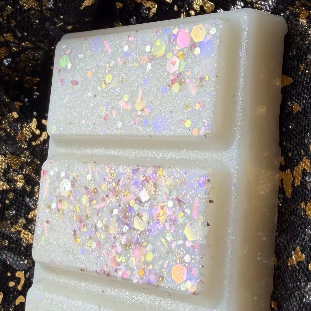 Close-up of the white Baby Mine baby powder scented soy wax melt segments decorated with multicoloured iridescent glitter.