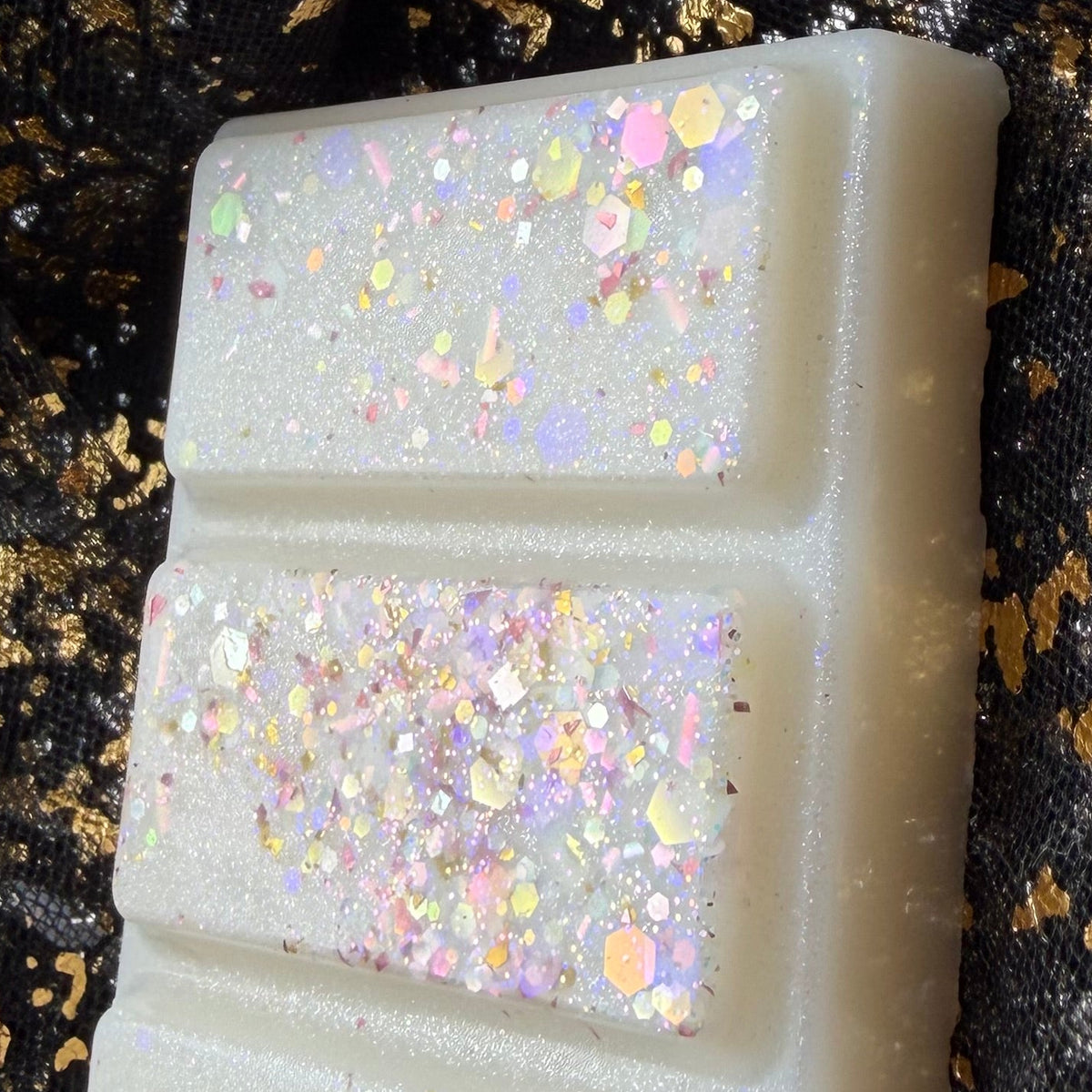 Close-up of the white Baby Mine baby powder scented soy wax melt segments decorated with multicoloured iridescent glitter.
