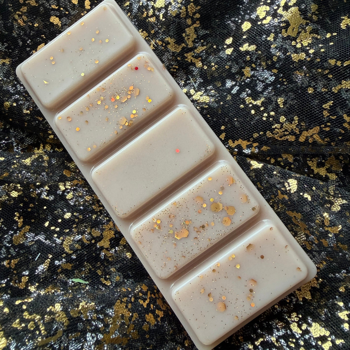 Sideways zoomed in image of the clamshell of The Library bookish wax melts showing shiny gold glitter and five-segment soy wax bar
